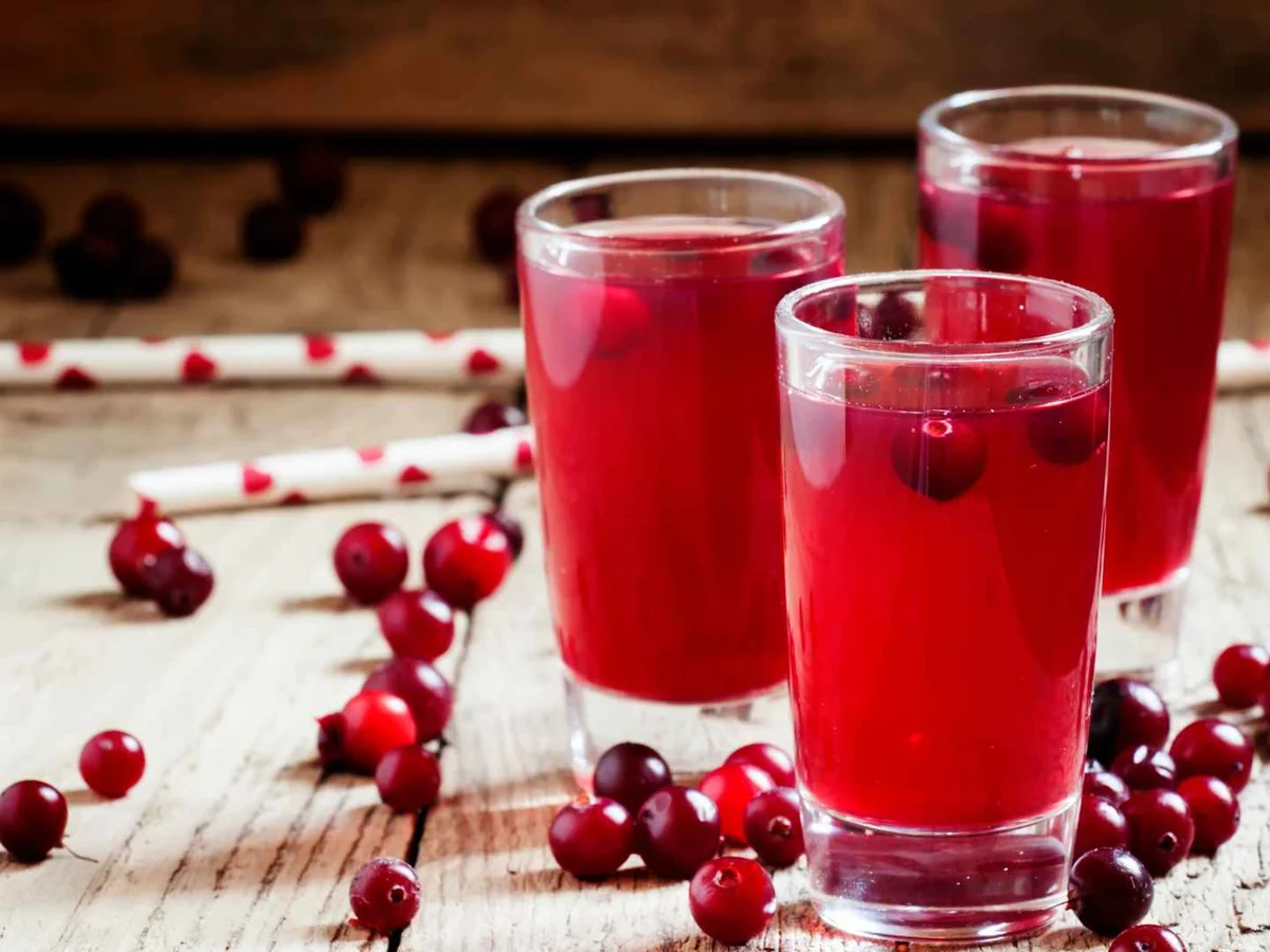 Three glasses of red cranberry drink with cranberries scattered nearby