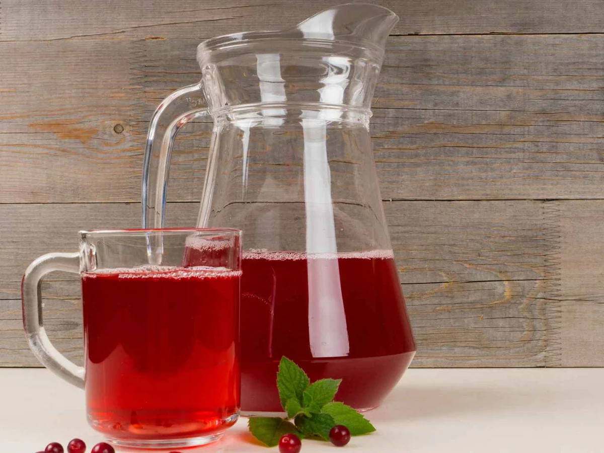 A glass mug and pitcher of red cranberry drink on a wooden table