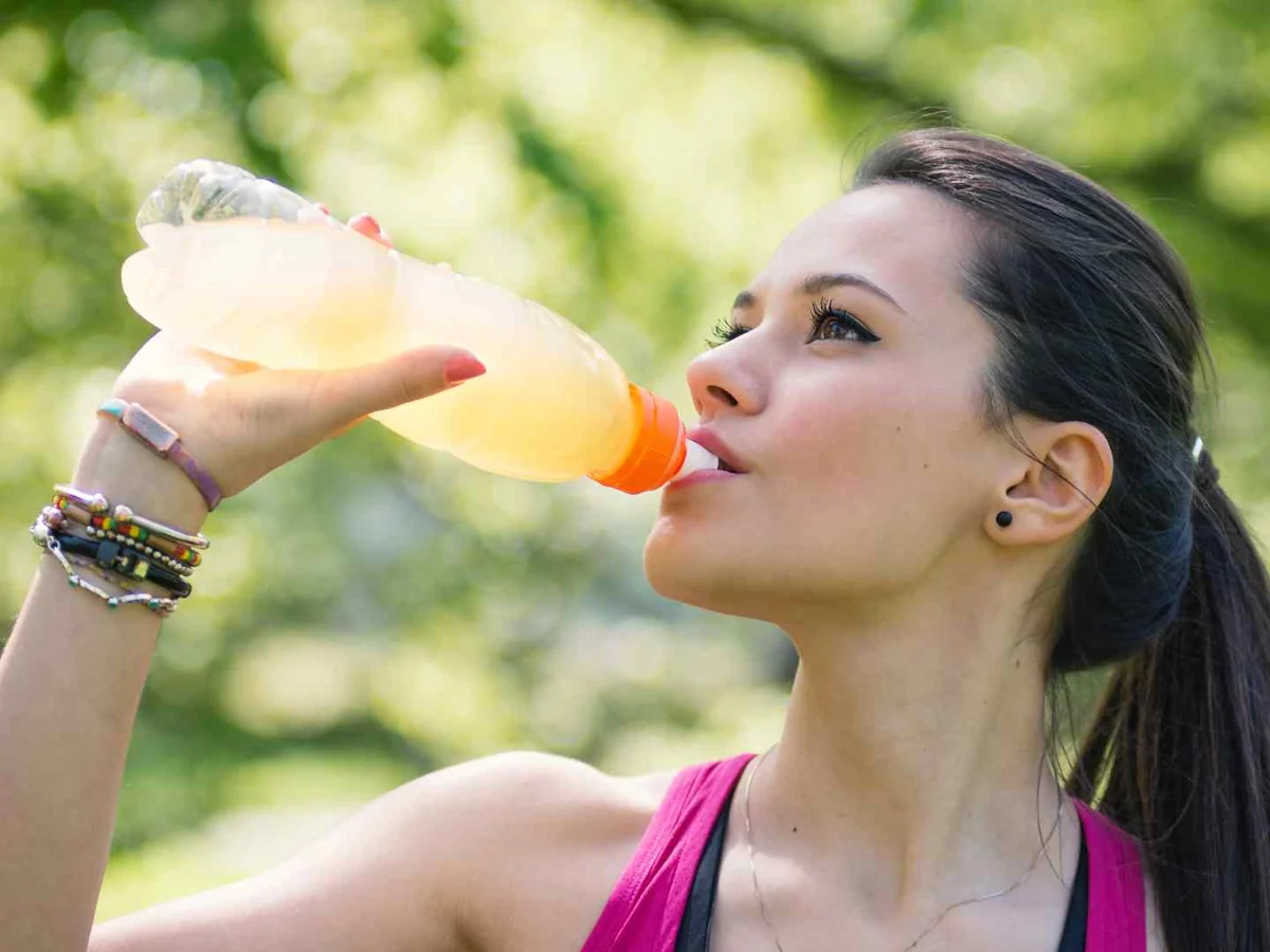 A woman drinking orange sports drink outdoors