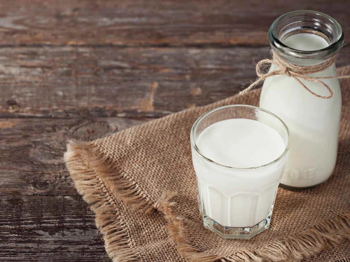 A glass and small bottle of milk on burlap over a rustic wooden table.