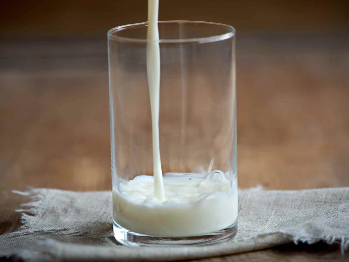 Milk pouring into a tall clear glass on a folded white cloth.
