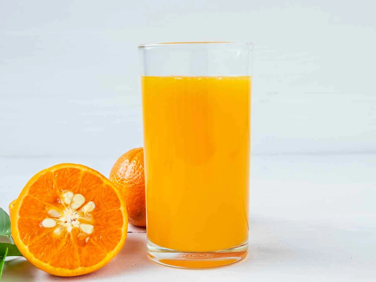 A tall glass of orange juice beside whole and halved oranges