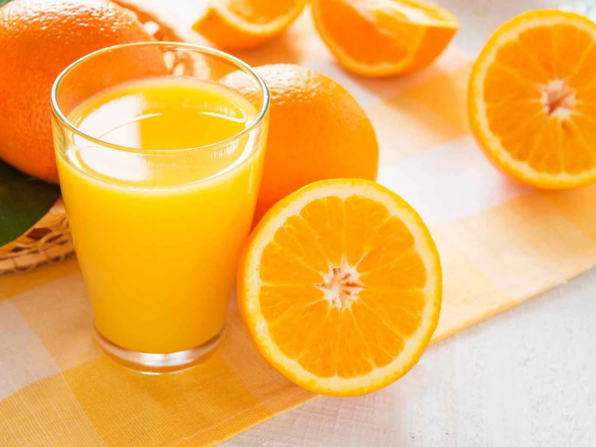 A glass of orange juice surrounded by whole and halved oranges