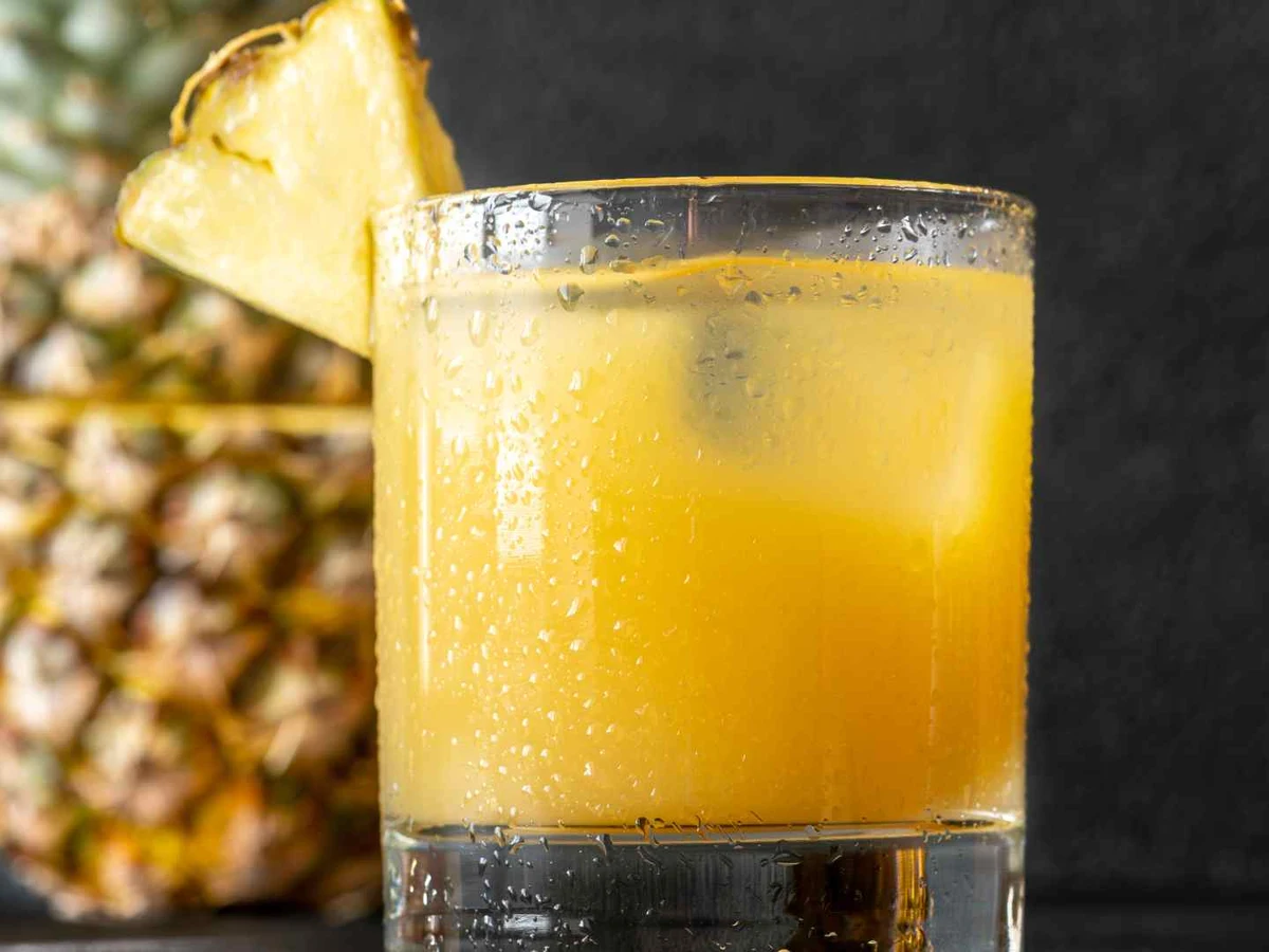 A glass of pineapple juice with bubbles and a pineapple wedge on the rim.
