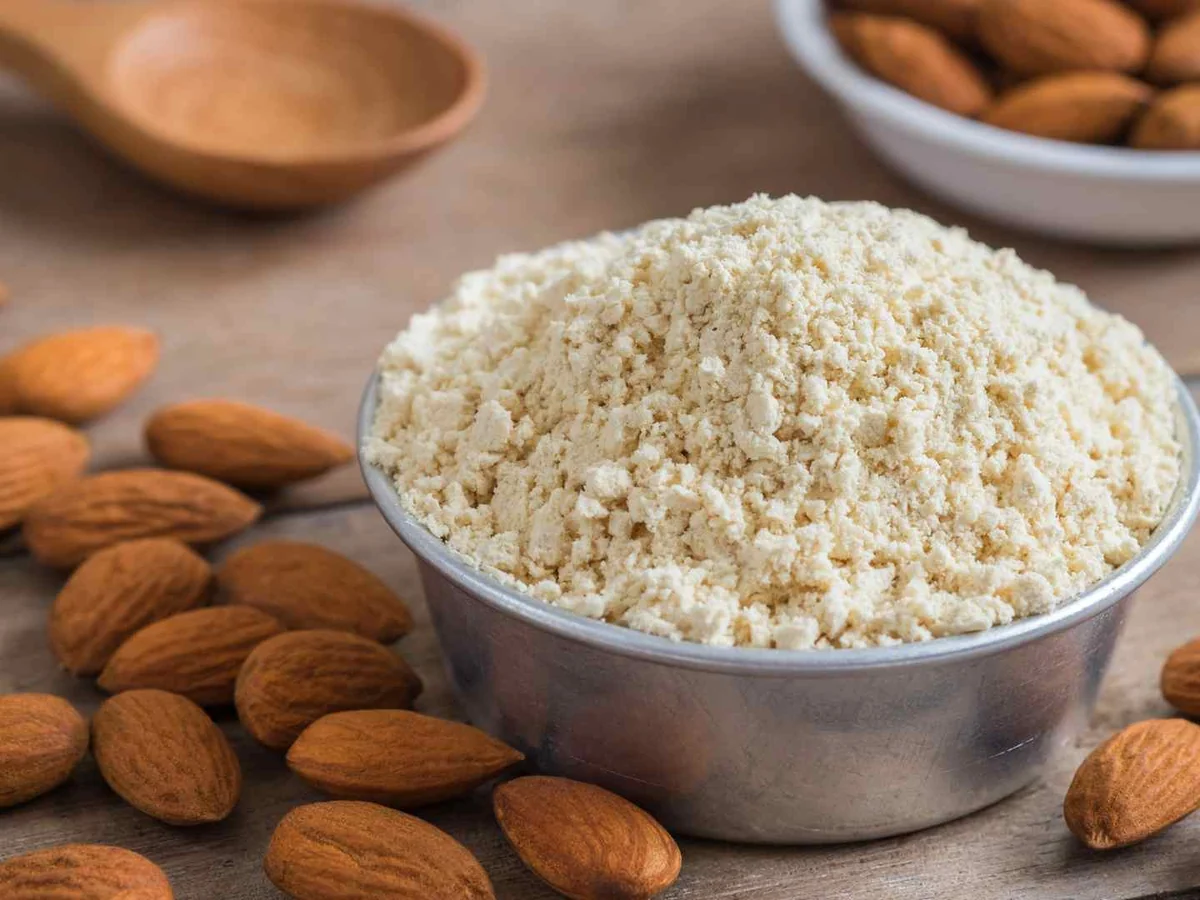 A metal bowl of almond flour surrounded by whole almonds