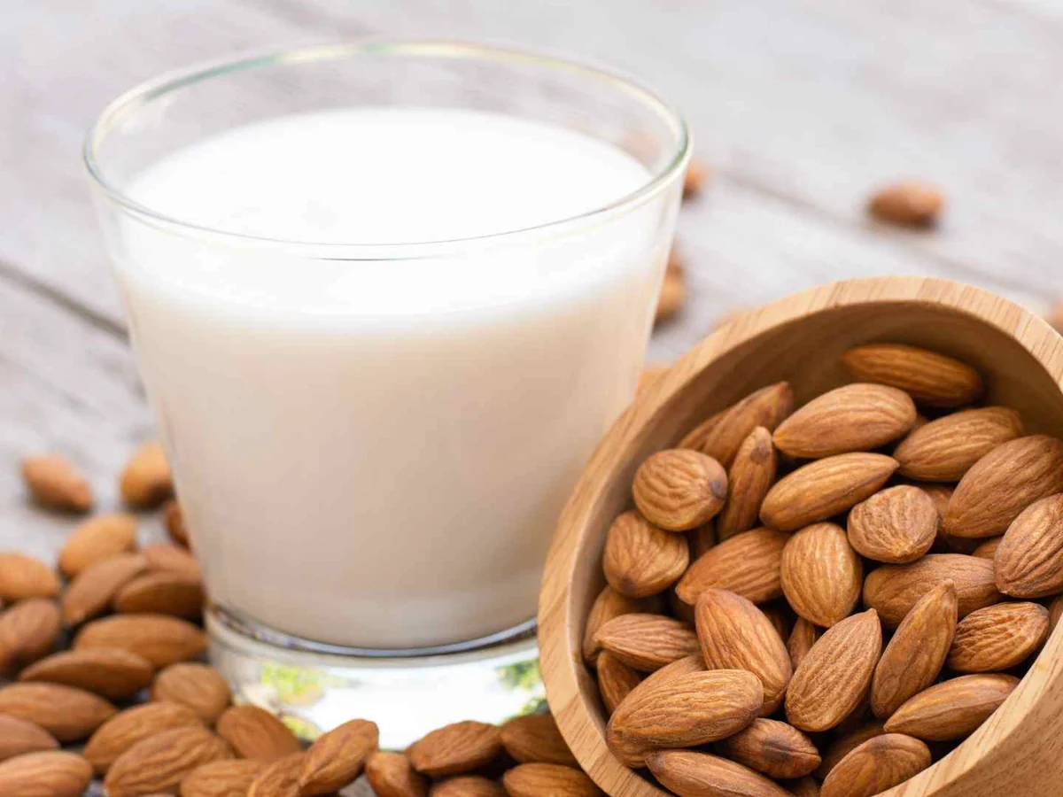 A glass of almond milk beside a wooden bowl of almonds
