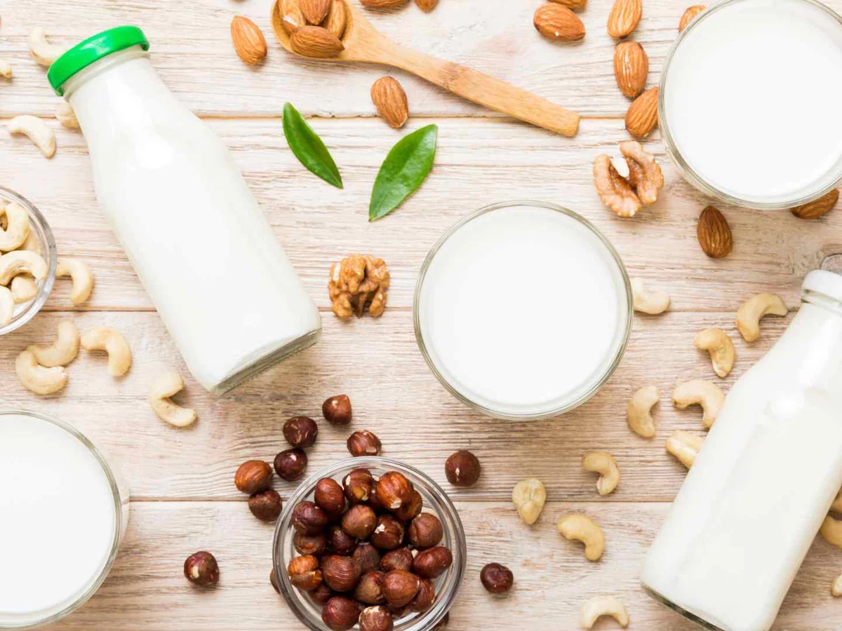 Several bottles and glasses of plant milk surrounded by mixed nuts