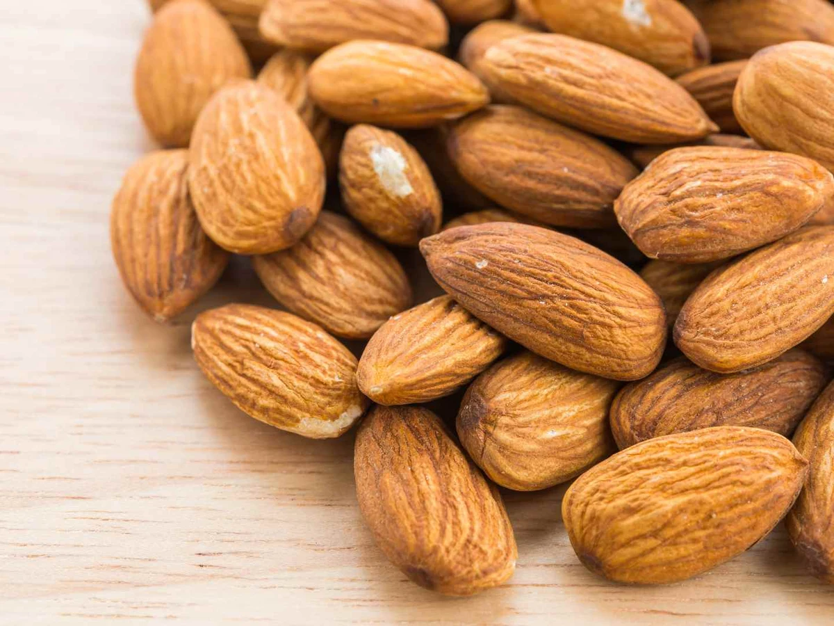 Loose whole almonds scattered across a pale wooden surface.