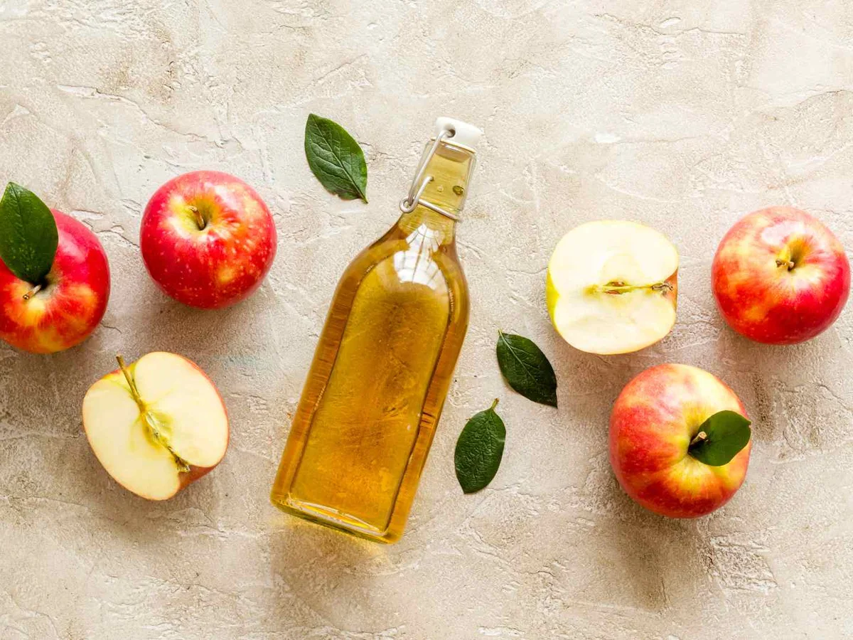 Apples, cut apple halves, and a bottle of amber vinegar arranged overhead.