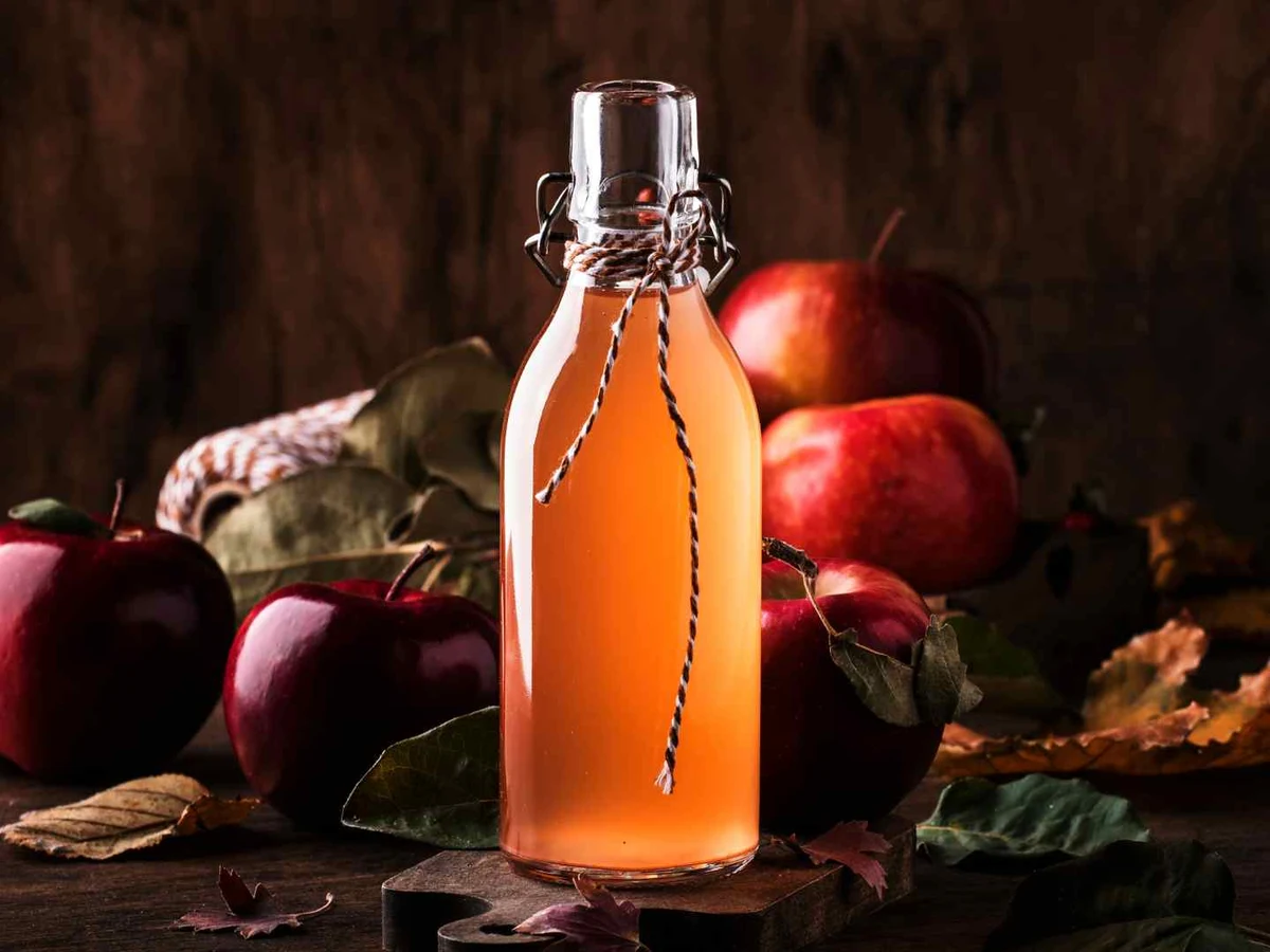A swing-top bottle of amber apple cider vinegar surrounded by apples.