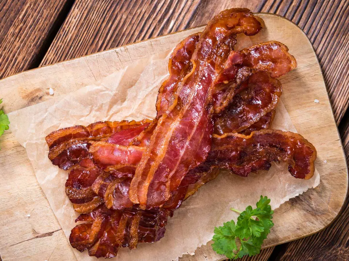 Crisp cooked bacon strips on parchment paper over a wooden board.