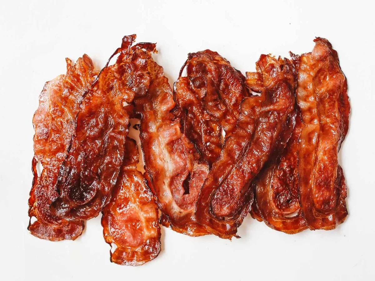 Dark crisp bacon strips arranged in a row on a white background.