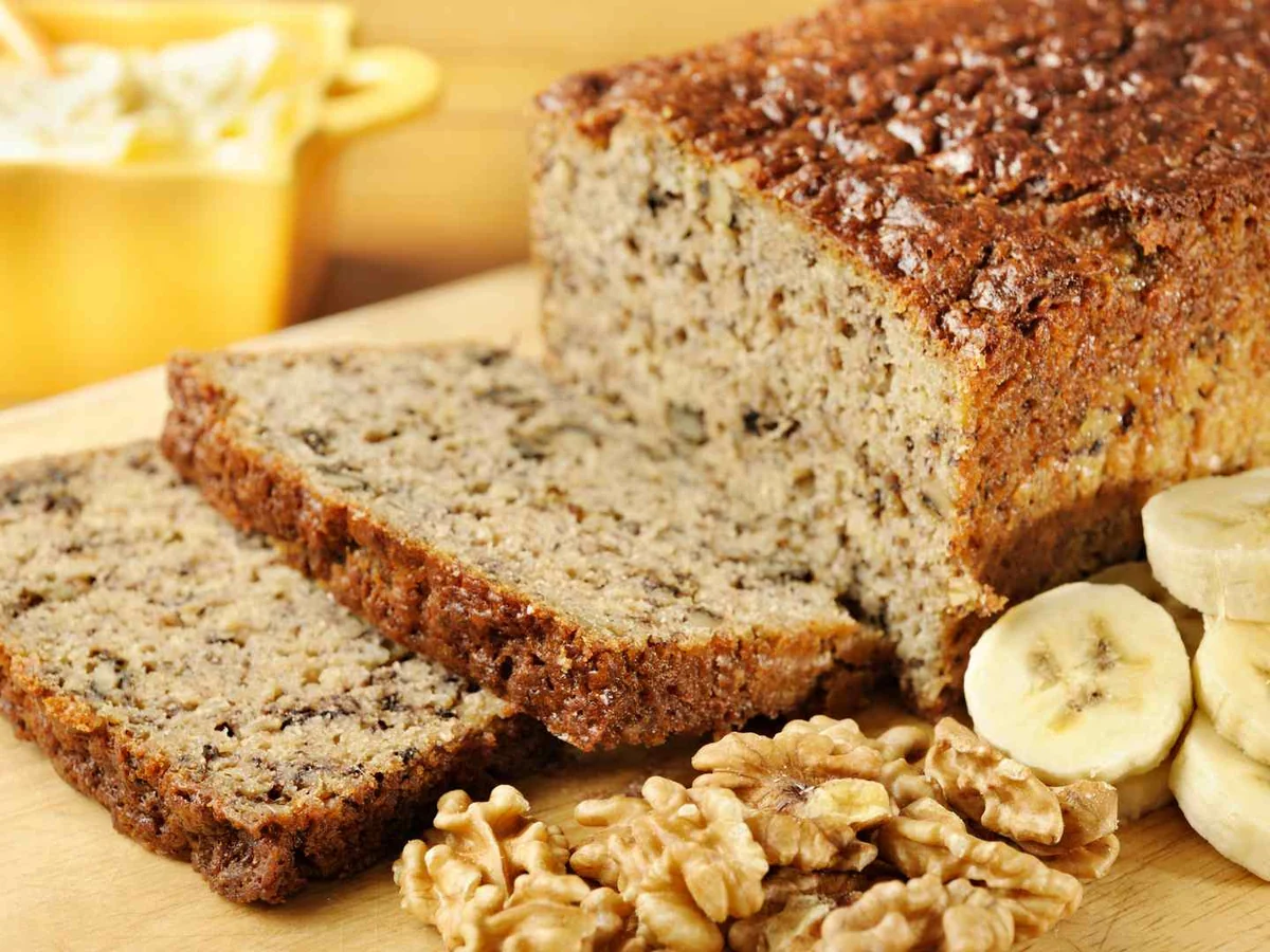 Banana bread slices beside bananas, walnuts, and a pat of butter