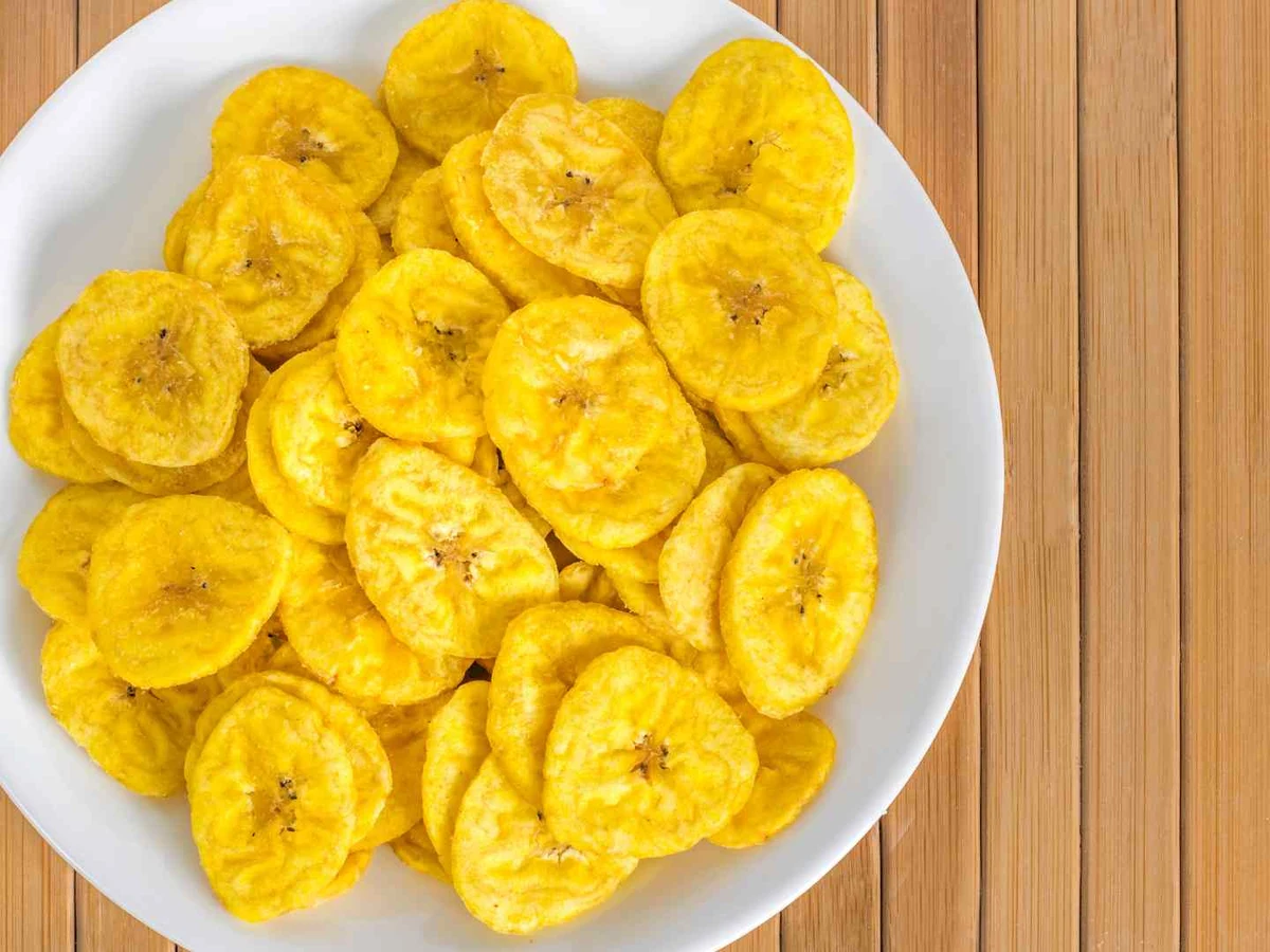 Banana chips in a white bowl viewed from above on a bamboo surface.