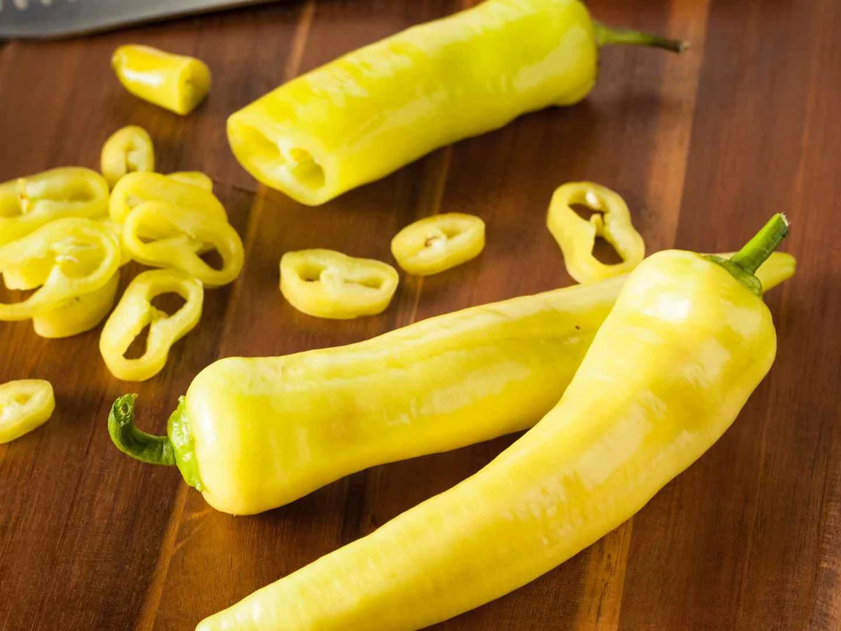 Whole and sliced pale yellow banana peppers on a wooden cutting board