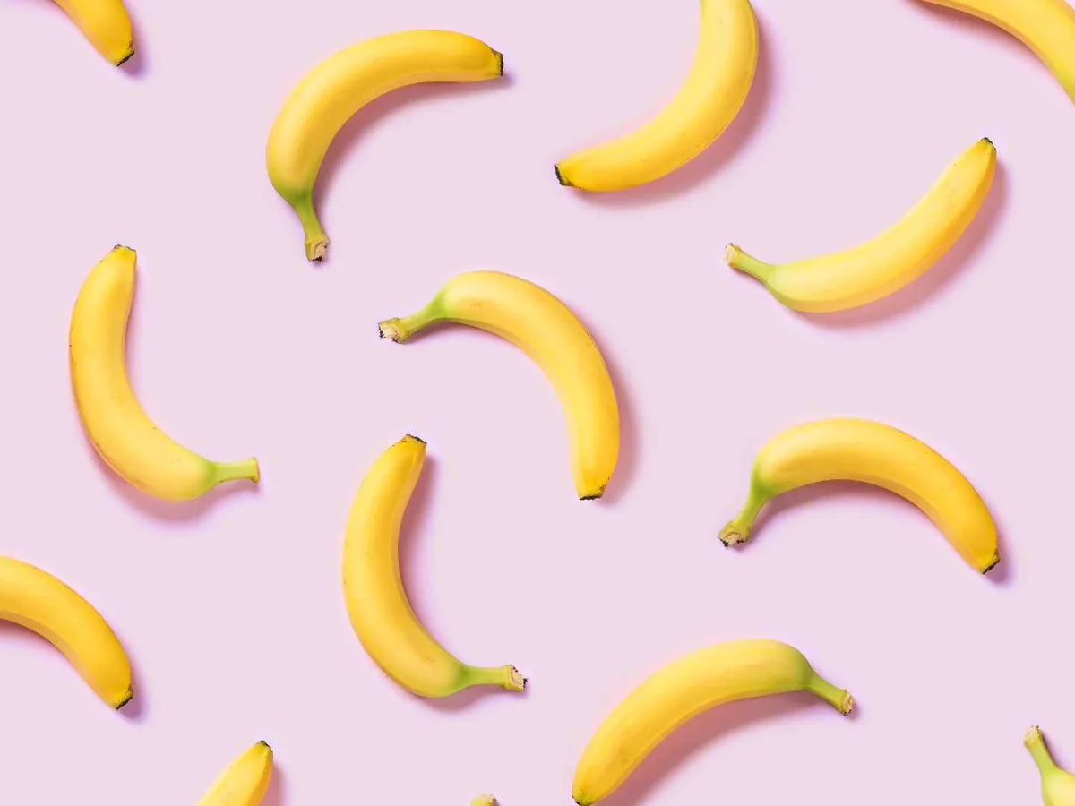 Whole yellow bananas arranged on a pale pink background