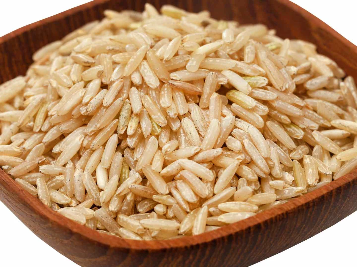 Uncooked brown basmati rice heaped in a wooden bowl on white.