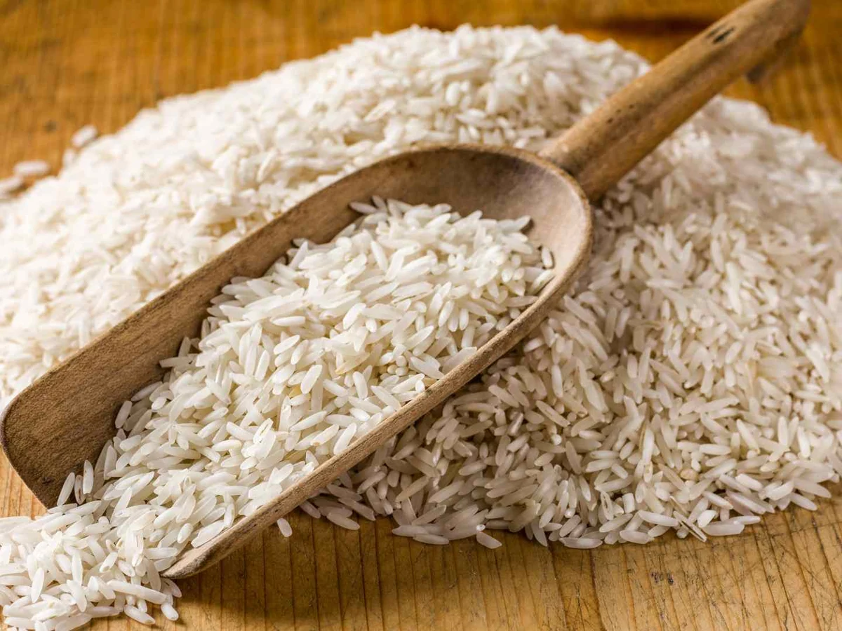Uncooked white basmati rice piled around a wooden scoop.