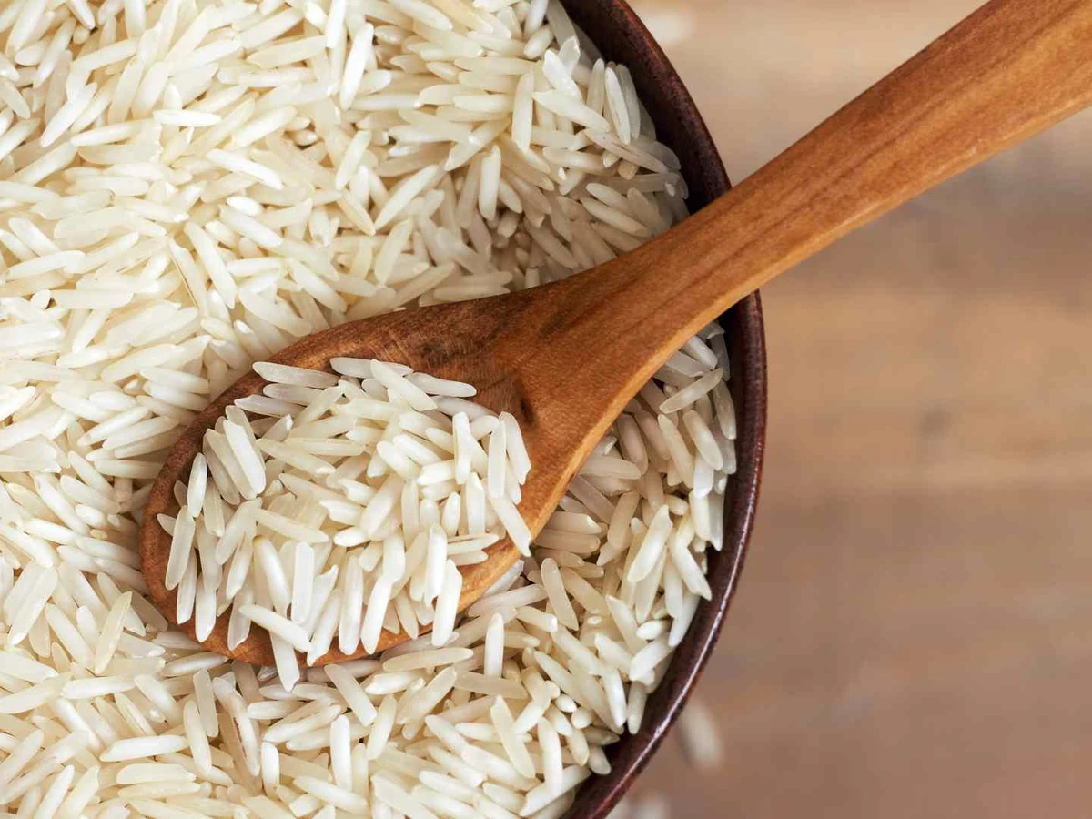 Uncooked white basmati rice in a wooden bowl with a wooden spoon.