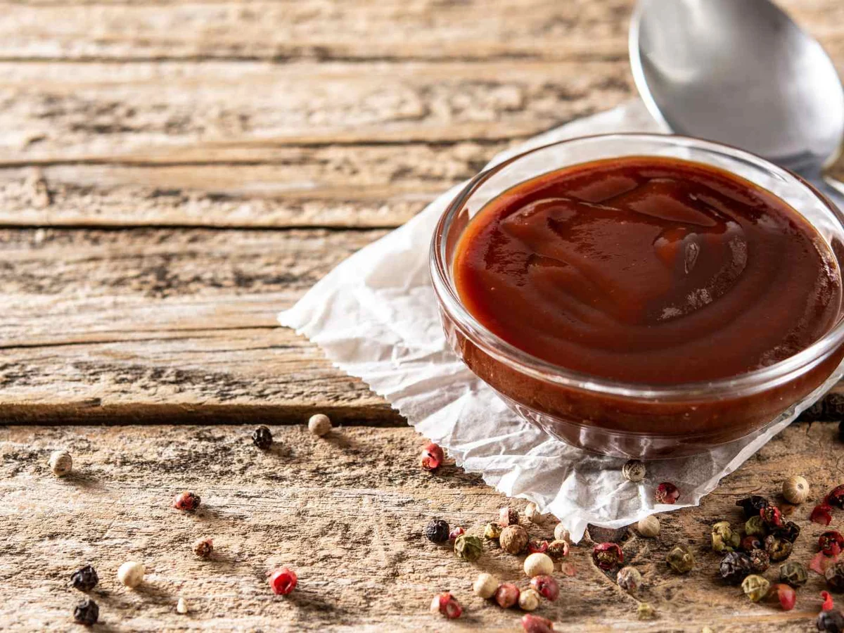 A small glass bowl of barbecue sauce with peppercorns nearby