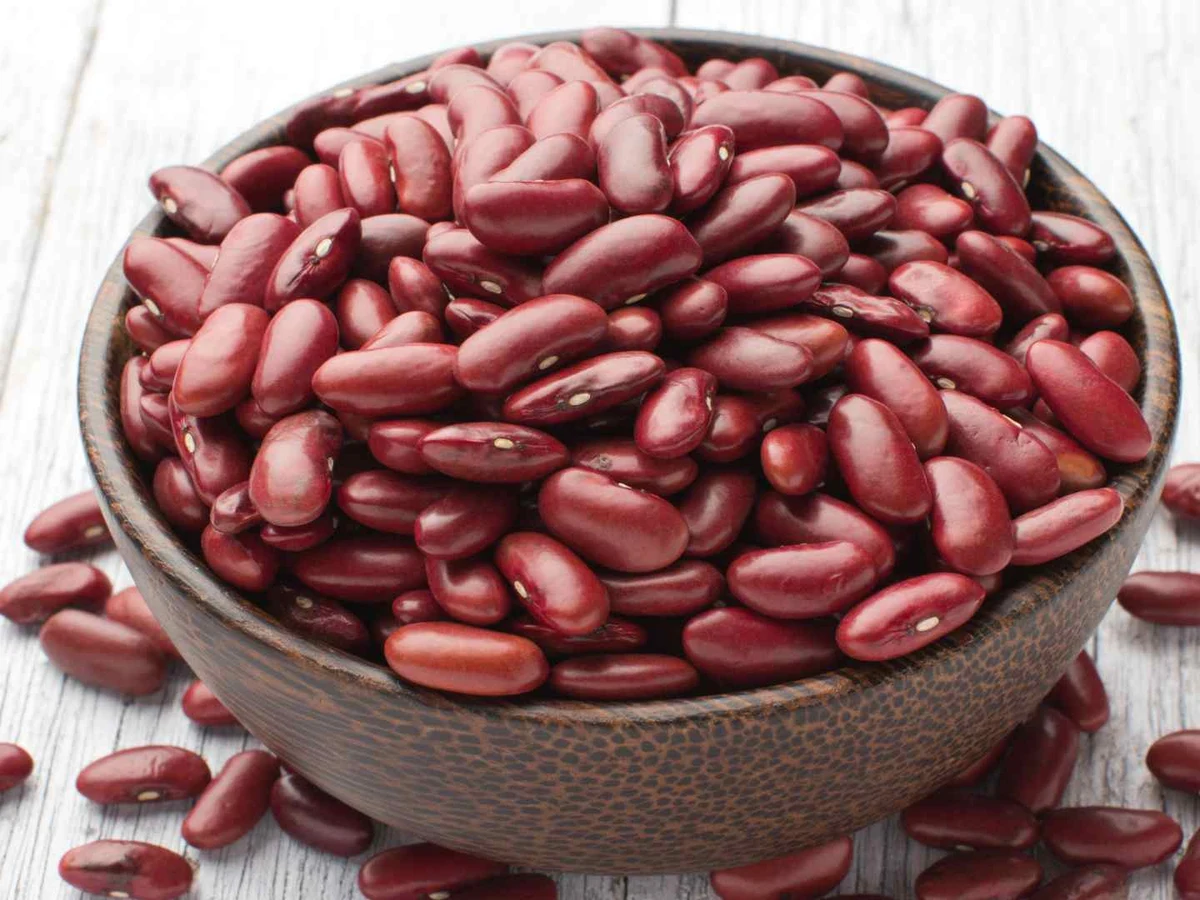 Red kidney beans fill a dark bowl with several beans scattered nearby.