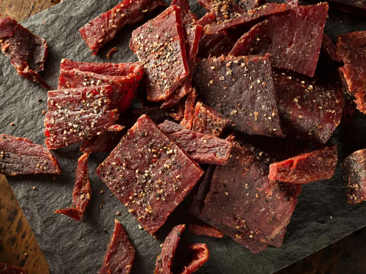 Thin rectangular beef jerky pieces scattered on a dark wooden board.