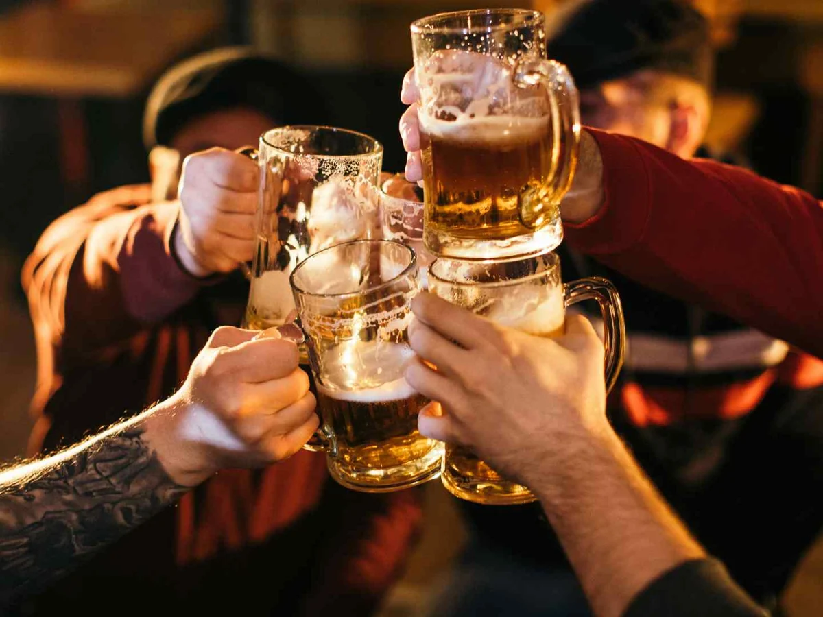 People clinking mugs of beer in a dim indoor setting