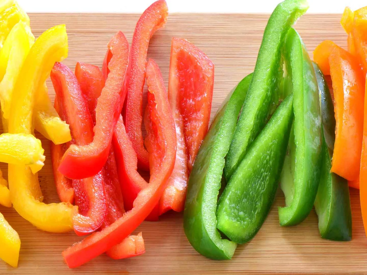 Red, yellow, orange, and green bell pepper strips on a cutting board