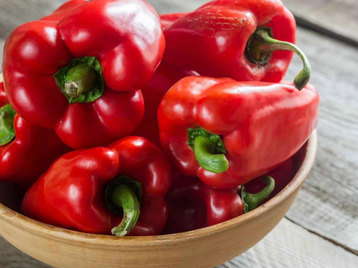Whole red bell peppers in a wooden bowl