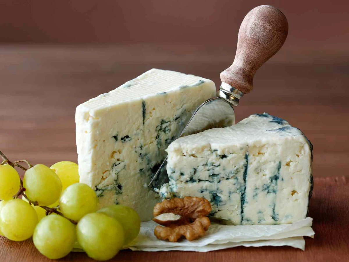 Three blocks of blue-veined cheese on a board with grapes and walnuts.