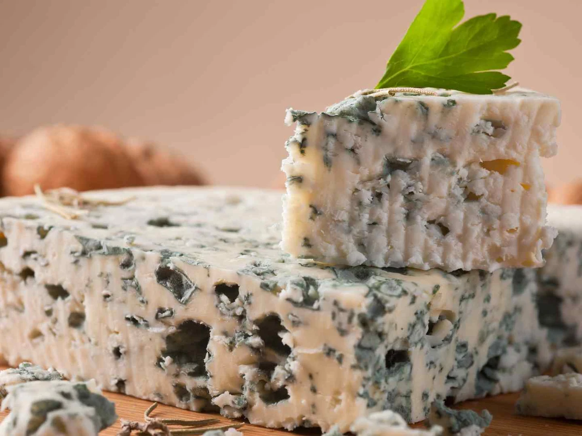 Several wedges of blue-veined cheese stacked on a wooden surface.