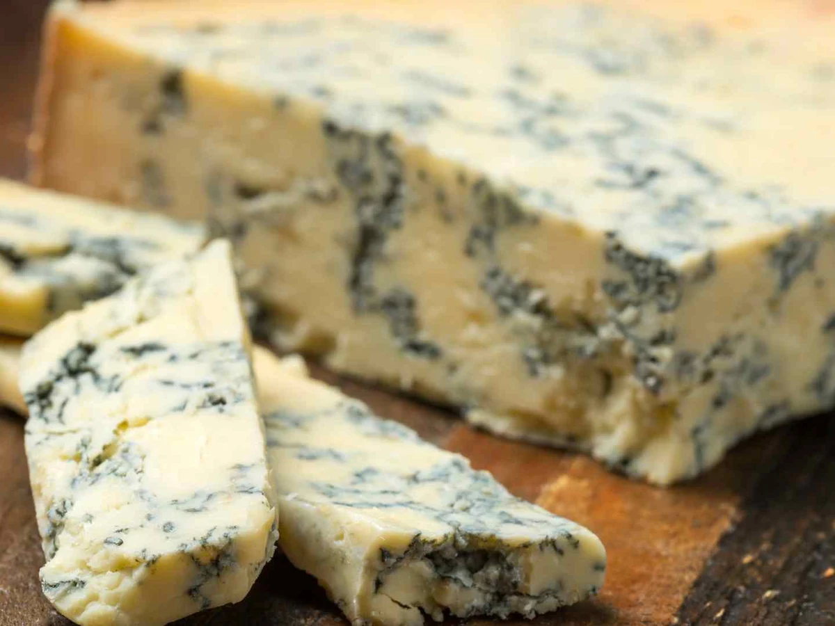 Blue cheese wedges and a larger block resting on a dark wooden board.