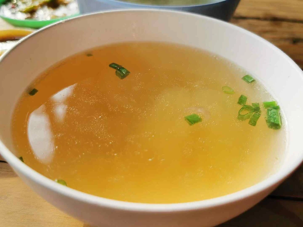 Clear golden broth in a white bowl topped with chopped green onion.