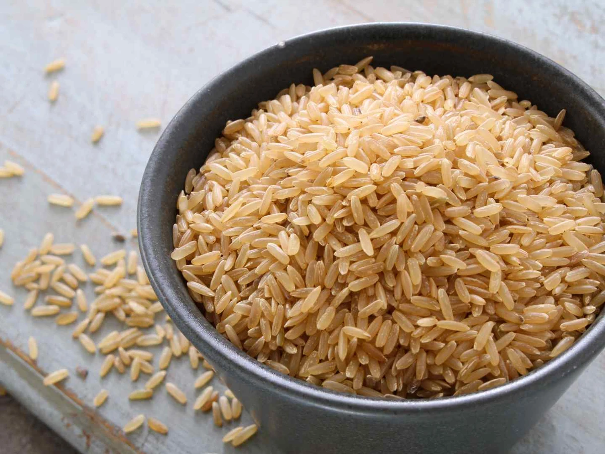 Uncooked brown rice in a dark bowl with loose grains nearby.