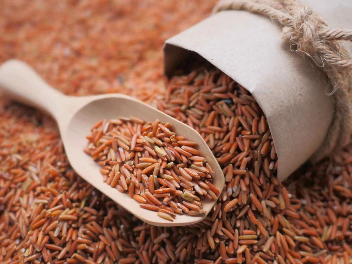 Reddish-brown rice spilling from a cloth sack around a wooden scoop.