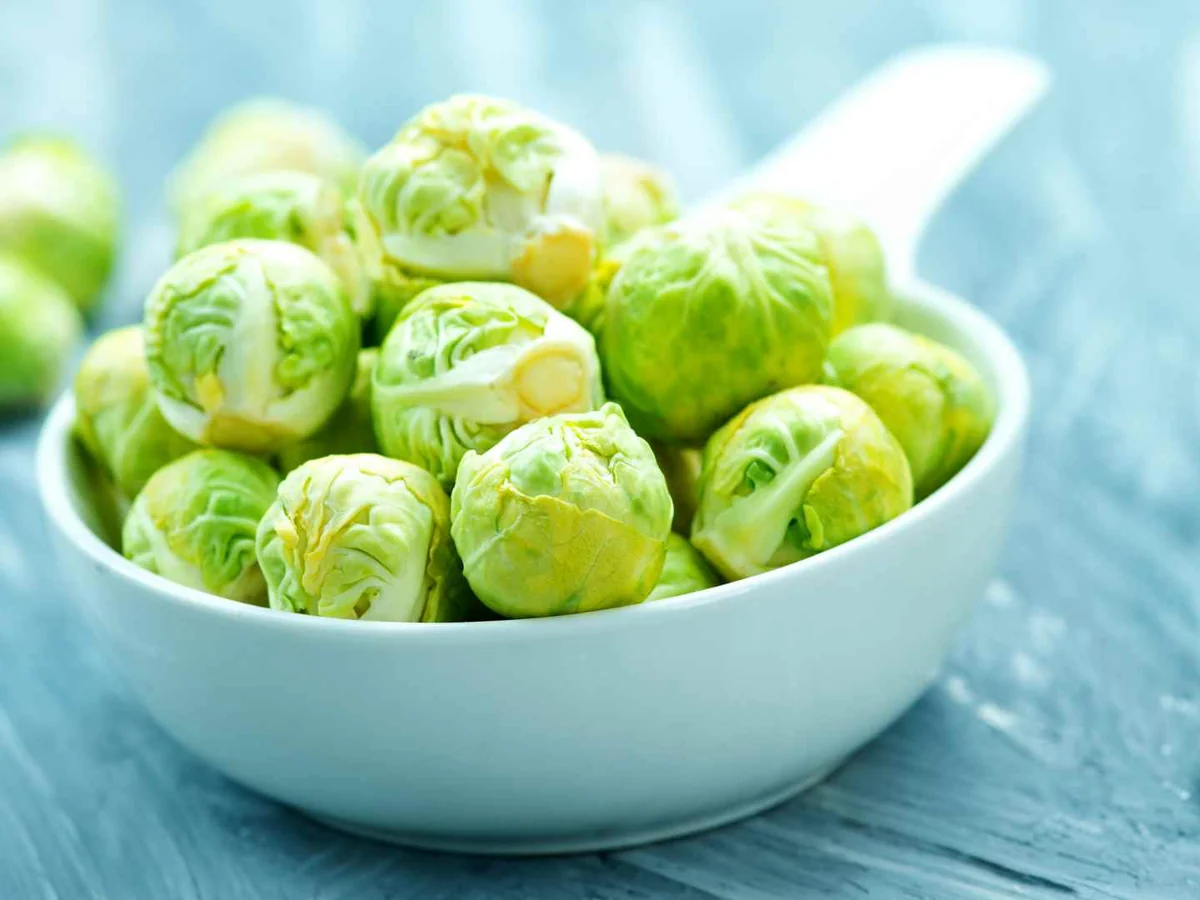 A white bowl of raw Brussels sprouts on a pale blue table