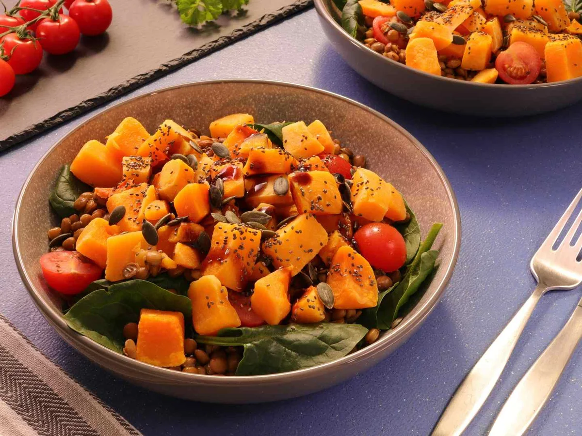 Bowls of roasted butternut squash cubes mixed with tomatoes and leafy greens.