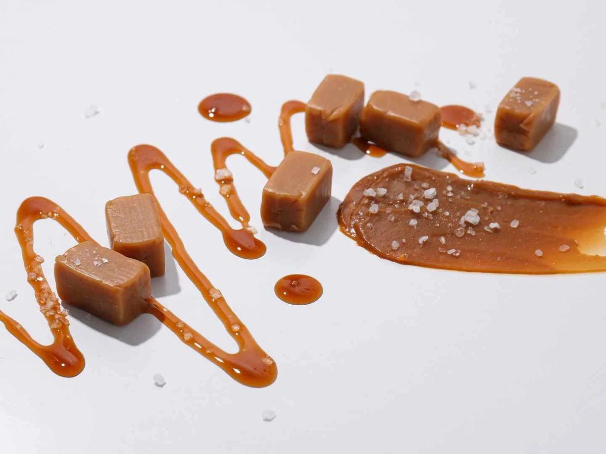 Caramel cubes, sauce drizzles, and coarse salt arranged on white.