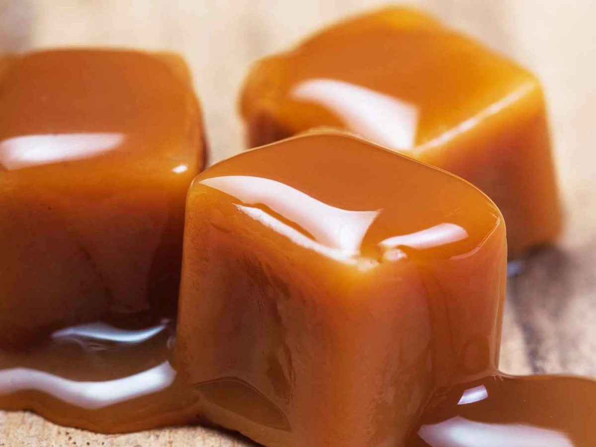 Three glossy caramel cubes sitting in a pool of caramel sauce.