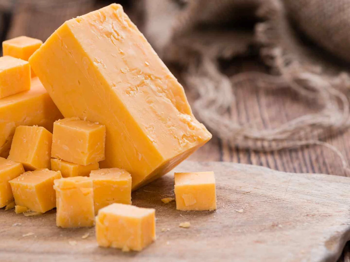 A block and cubes of orange cheddar cheese on a wooden board