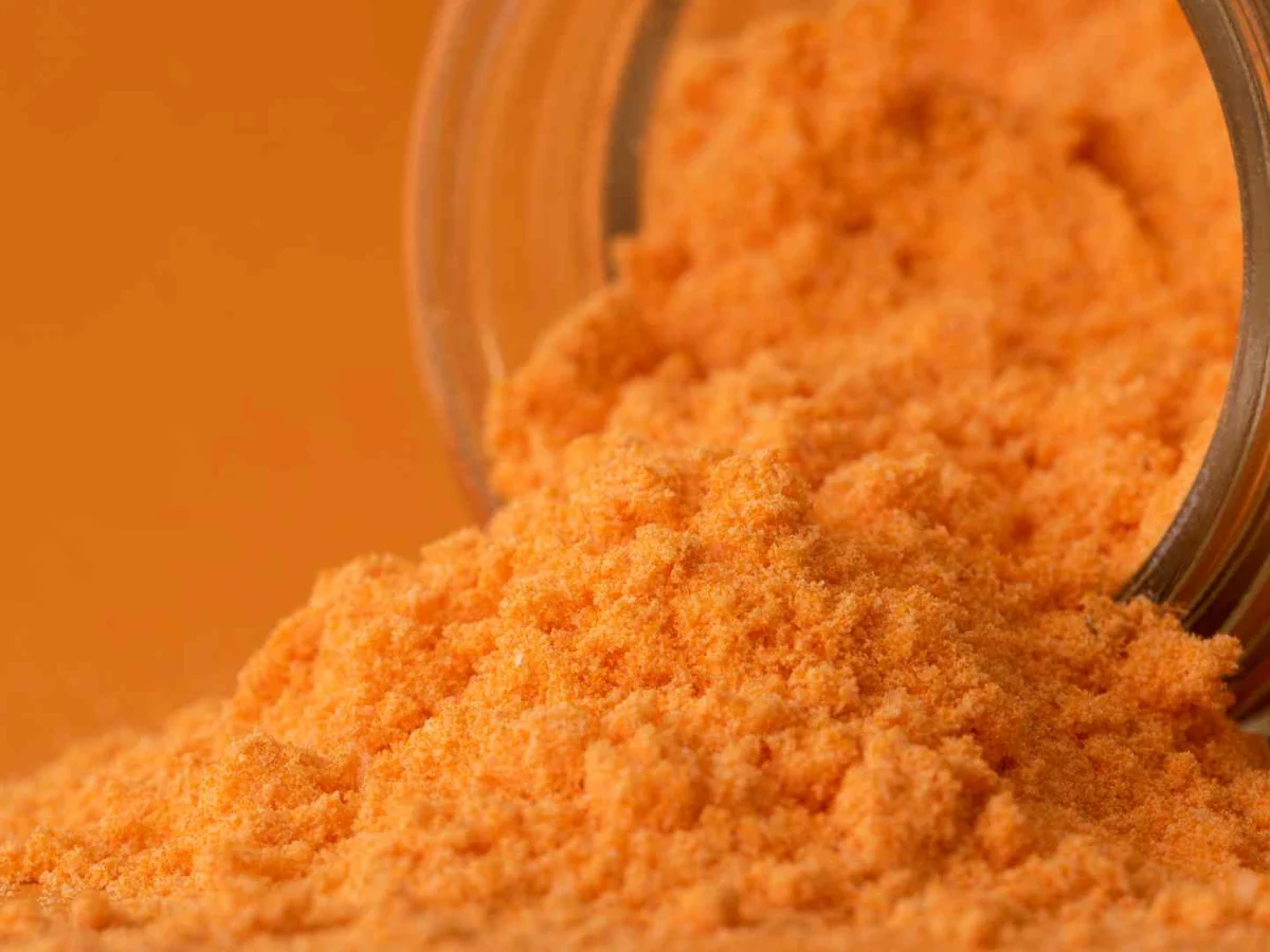 Orange cheddar cheese powder spilling from a glass jar