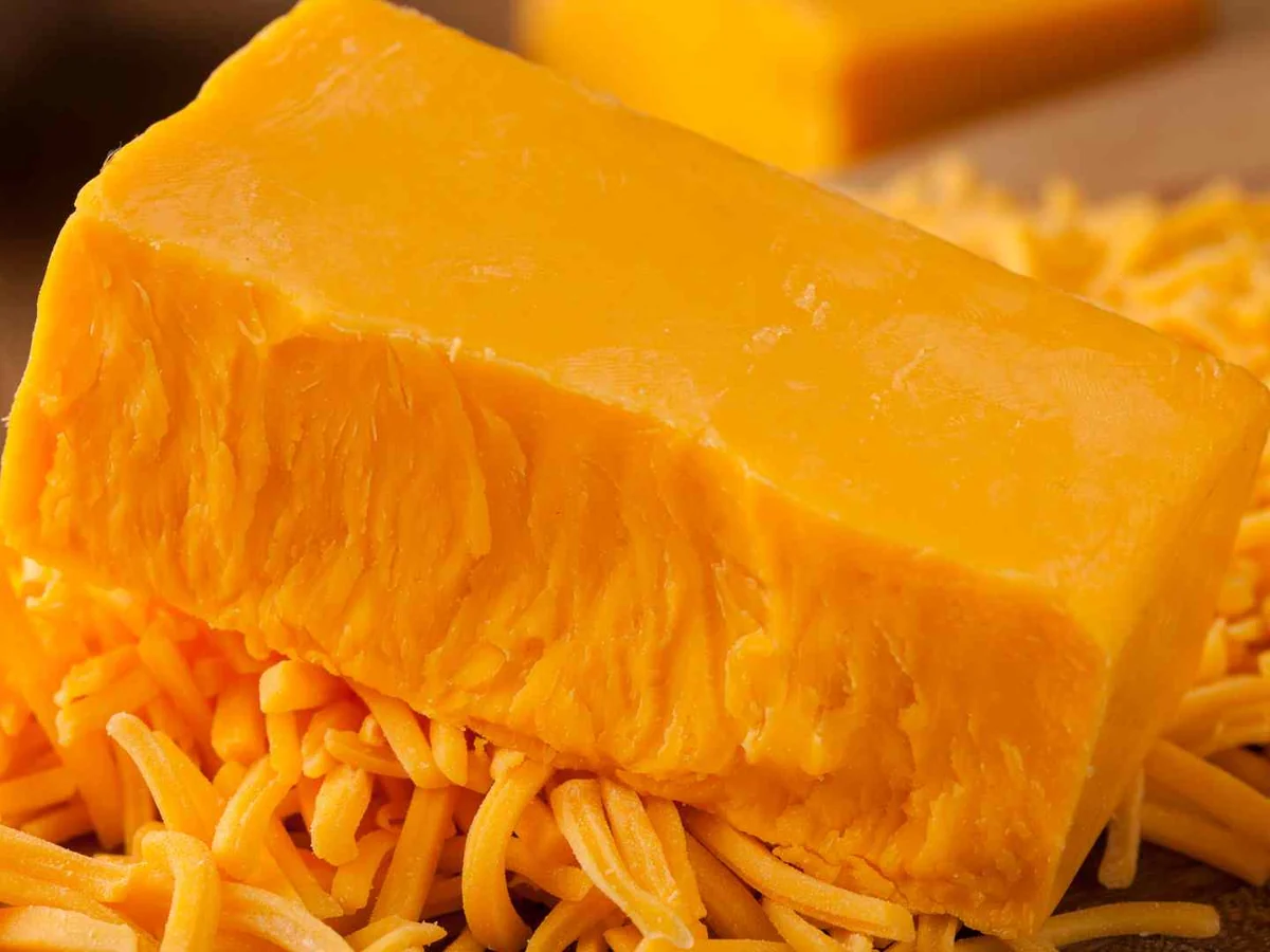 A block of orange cheddar resting on shredded cheese
