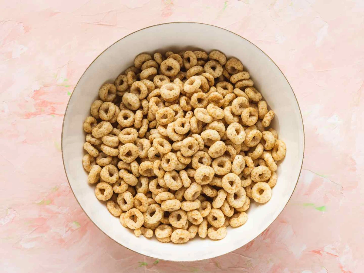 A bowl of plain oat cereal rings viewed from above on a pink surface.