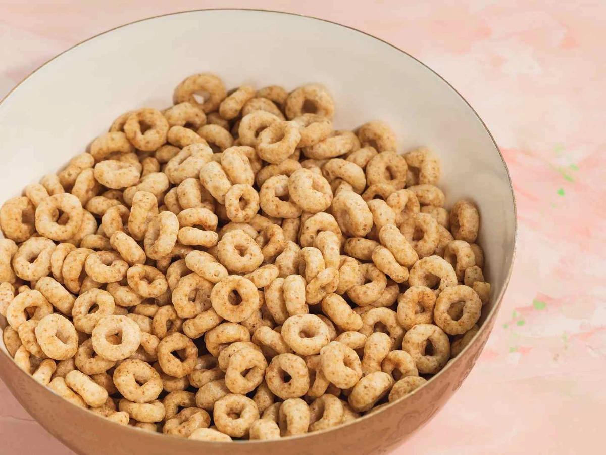 A glass bowl filled with plain oat cereal rings on a pink surface.