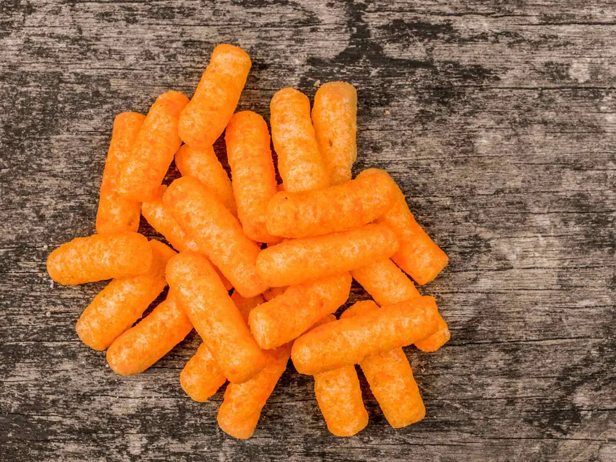 A small pile of orange cheese snacks on a dark wooden surface