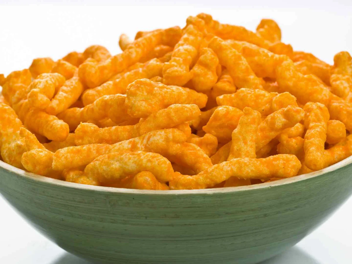 A green bowl overflowing with orange cheese snacks on white