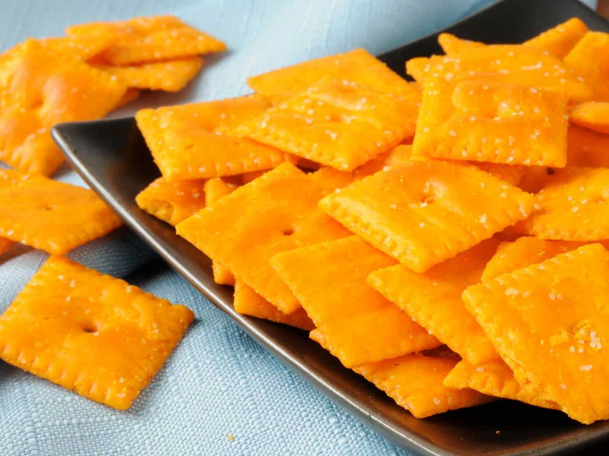 Orange square cheese crackers piled on two black plates.