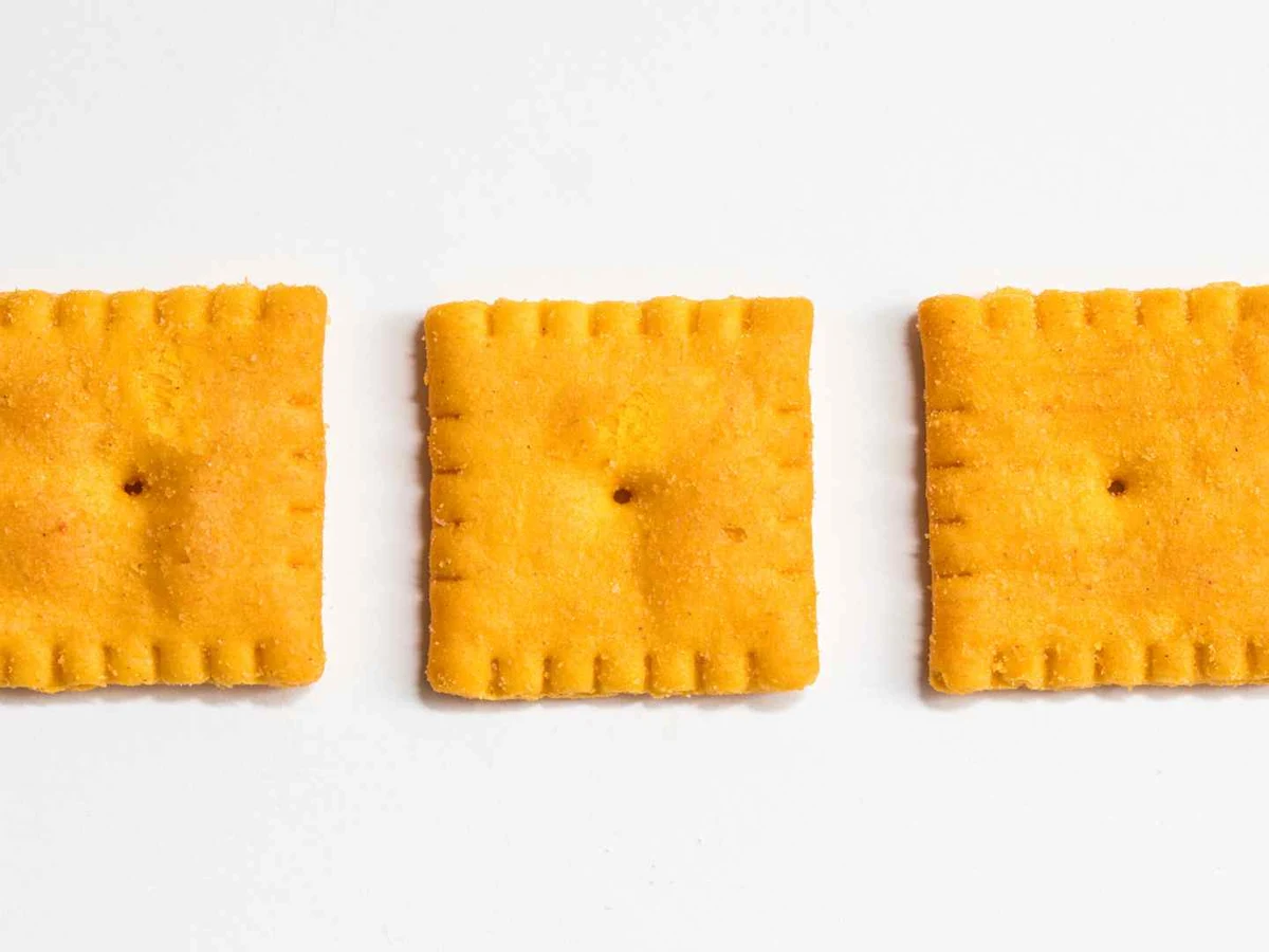 Three orange square cheese crackers arranged in a row on white.