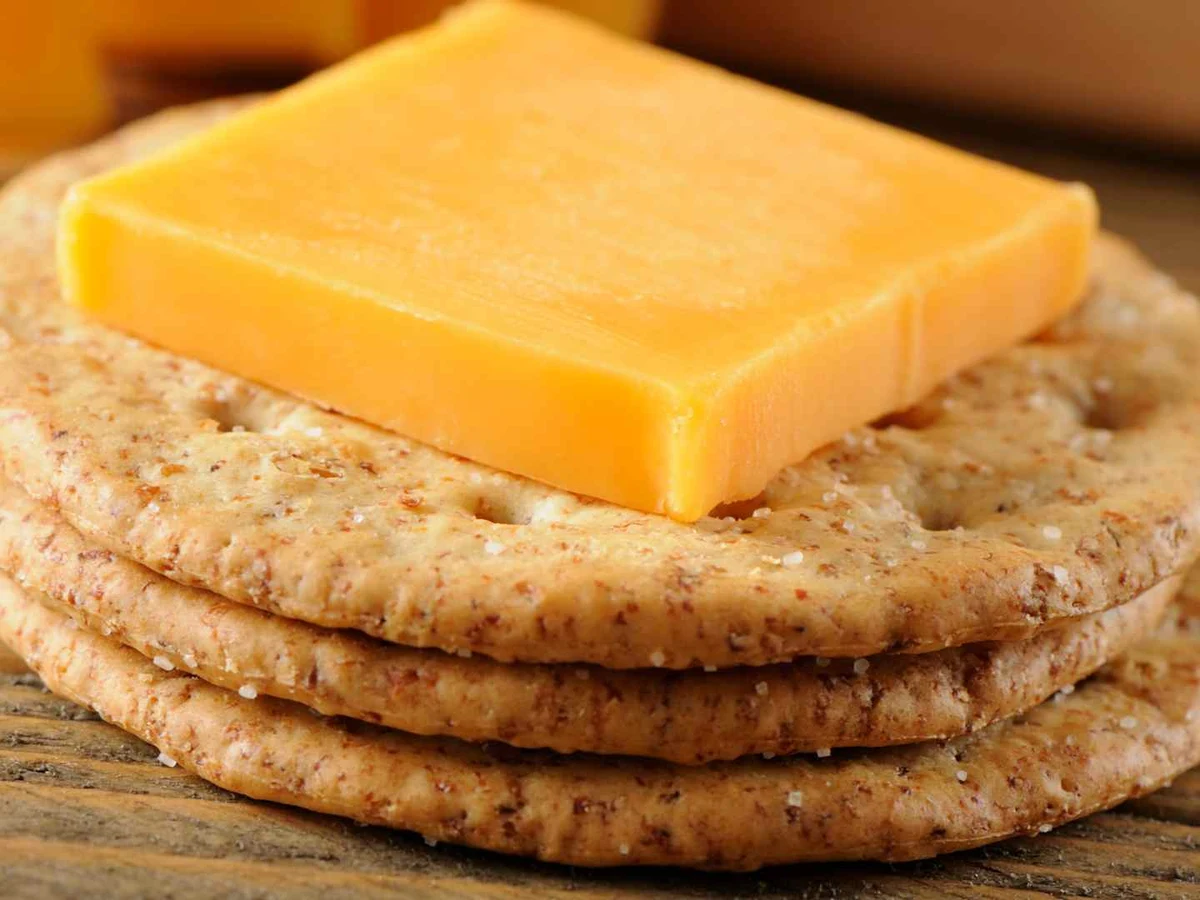 Orange cheese crackers topped by a block of cheddar on round wheat crackers.