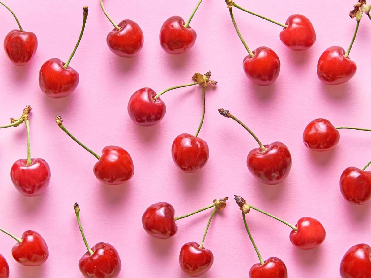 Individual red cherries with stems arranged across a pink background
